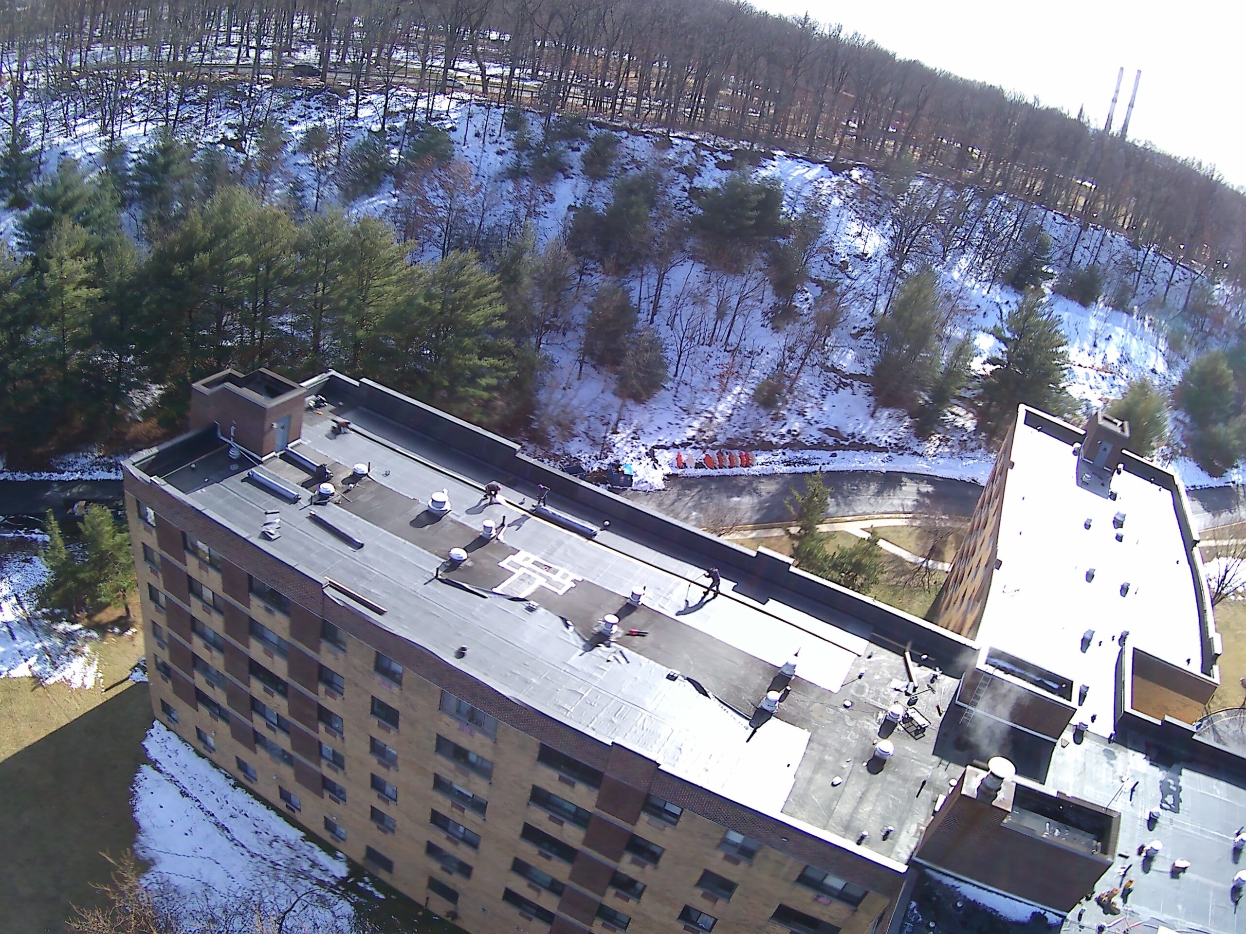 Aerial view of a large low-slope commercial roof beside a parking lot