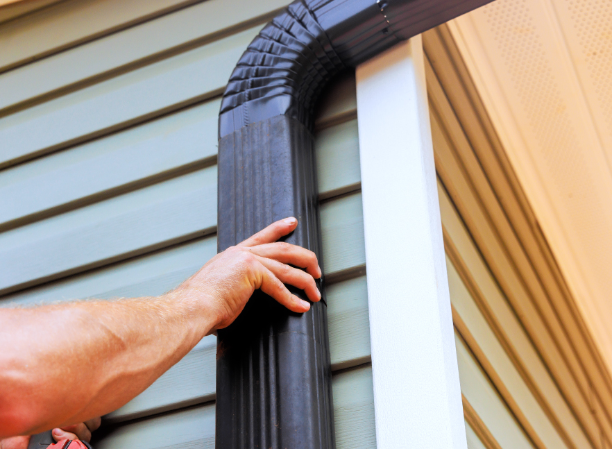Detail of a downspout fitted to a home’s corner over tan siding