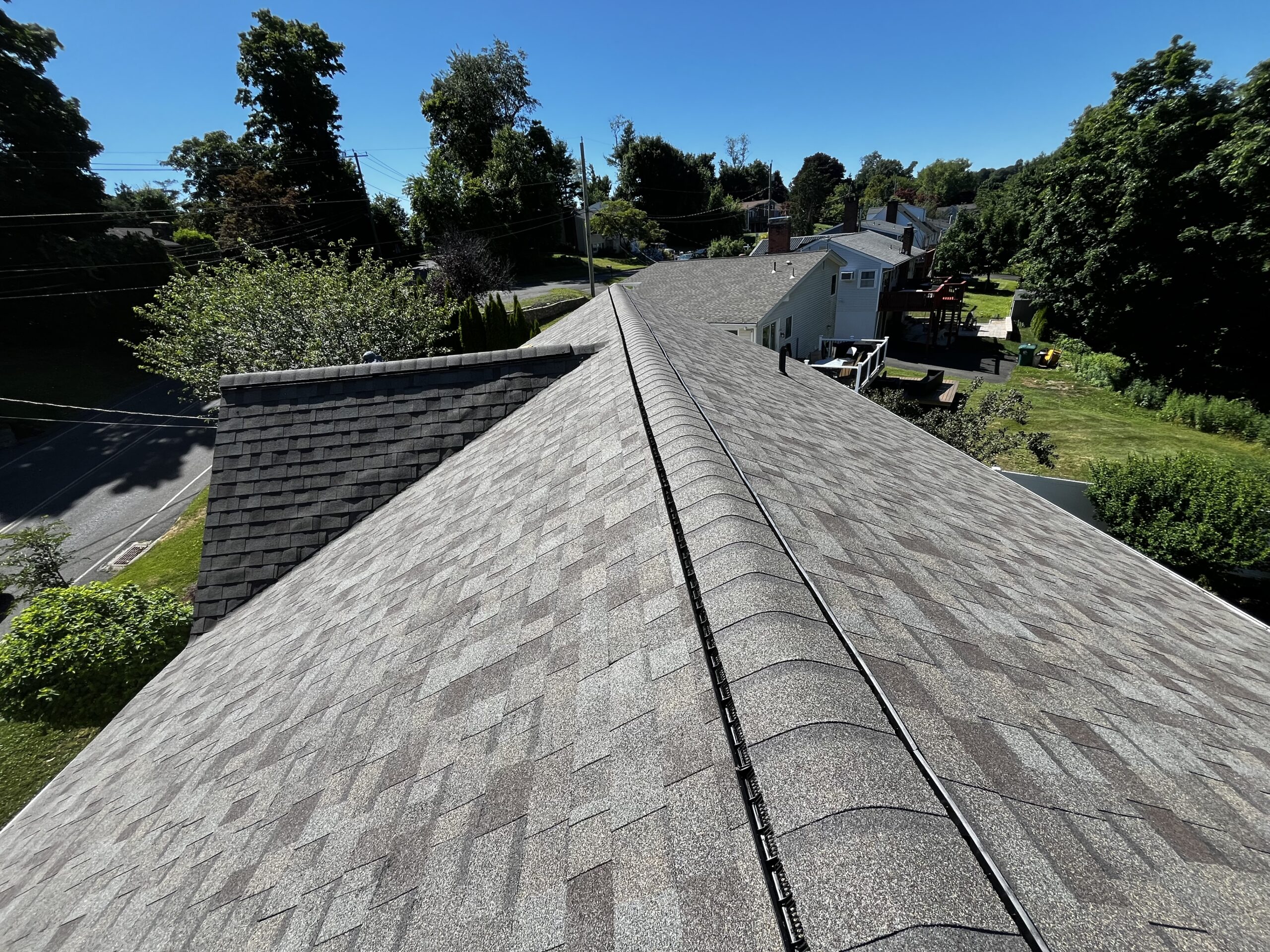 View standing on a finished roof ridge, looking down a crisp shingle course over a Connecticut neighborhood