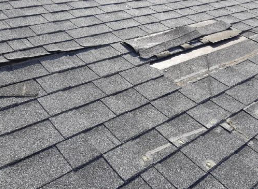 Close-up of aging, storm-worn asphalt shingles with a lifted, curling tab