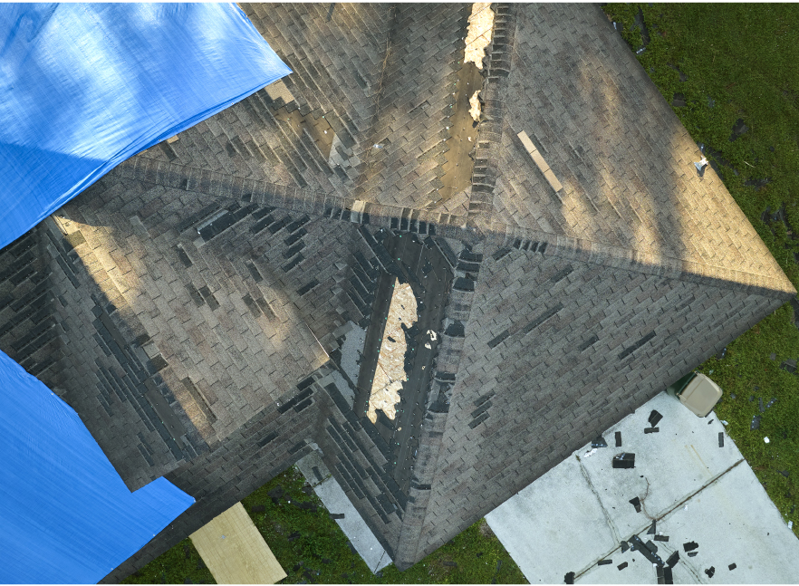 Aerial view of a steep roof with an emergency blue tarp installed after storm damage — Everett Construction storm response